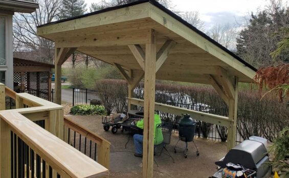 Covered wooden patio with seating and grill.