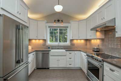 Modern kitchen with white cabinets, stainless steel appliances, and farmhouse sink under window.
