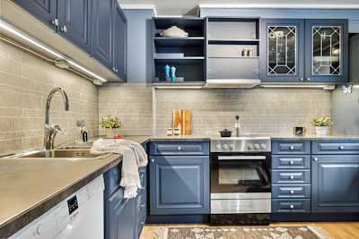 Stylish kitchen with bold blue cabinets, stainless steel appliances, and glass-front shelving.